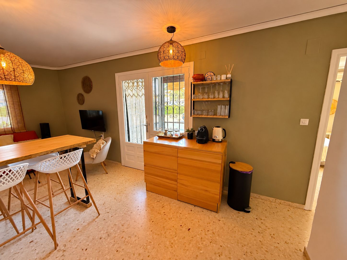 Cocina compacta con una isla de madera, taburetes de bar, un televisor y una mesa de comedor.