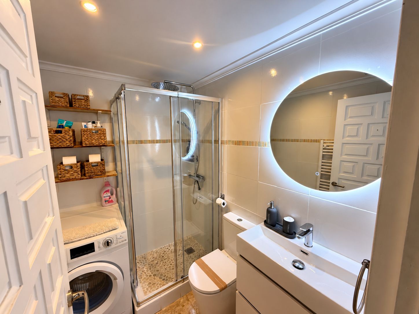A modern bathroom with a glass-enclosed shower, a toilet, a sink, and a mirror.