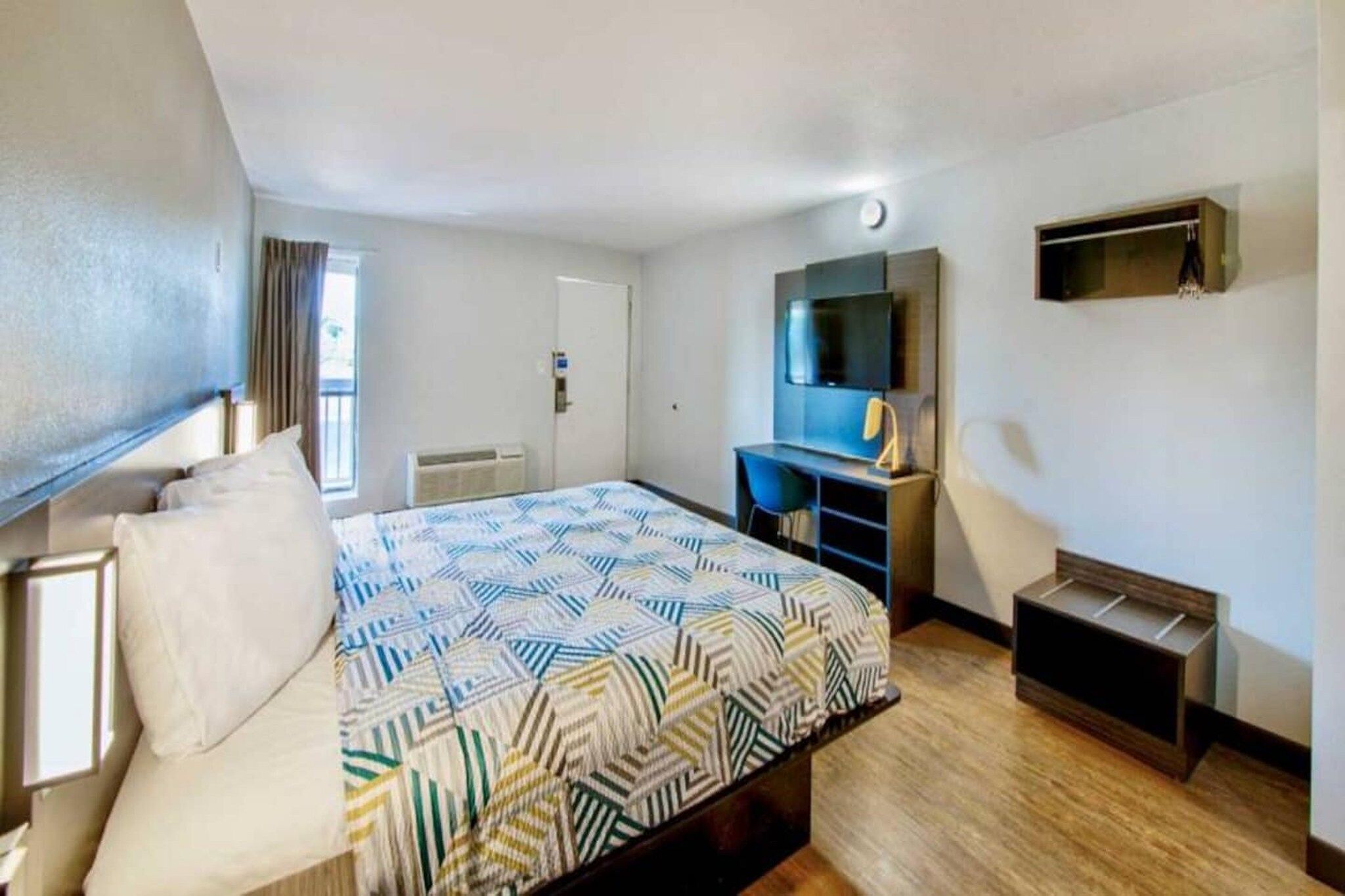 A hotel room with a bed, a desk, a chair, a TV, and a wardrobe.