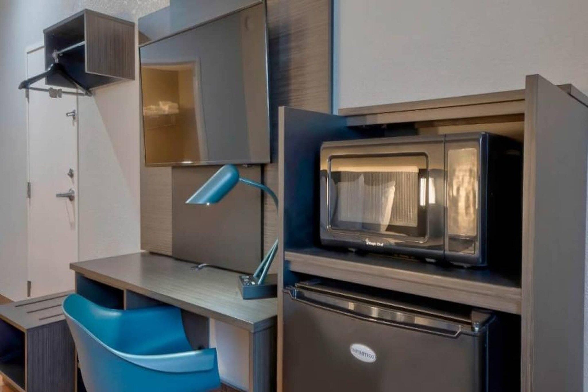 Eine kleine Küchenzeile mit einer Mikrowelle, einem Kühlschrank und einem blauen Stuhl.