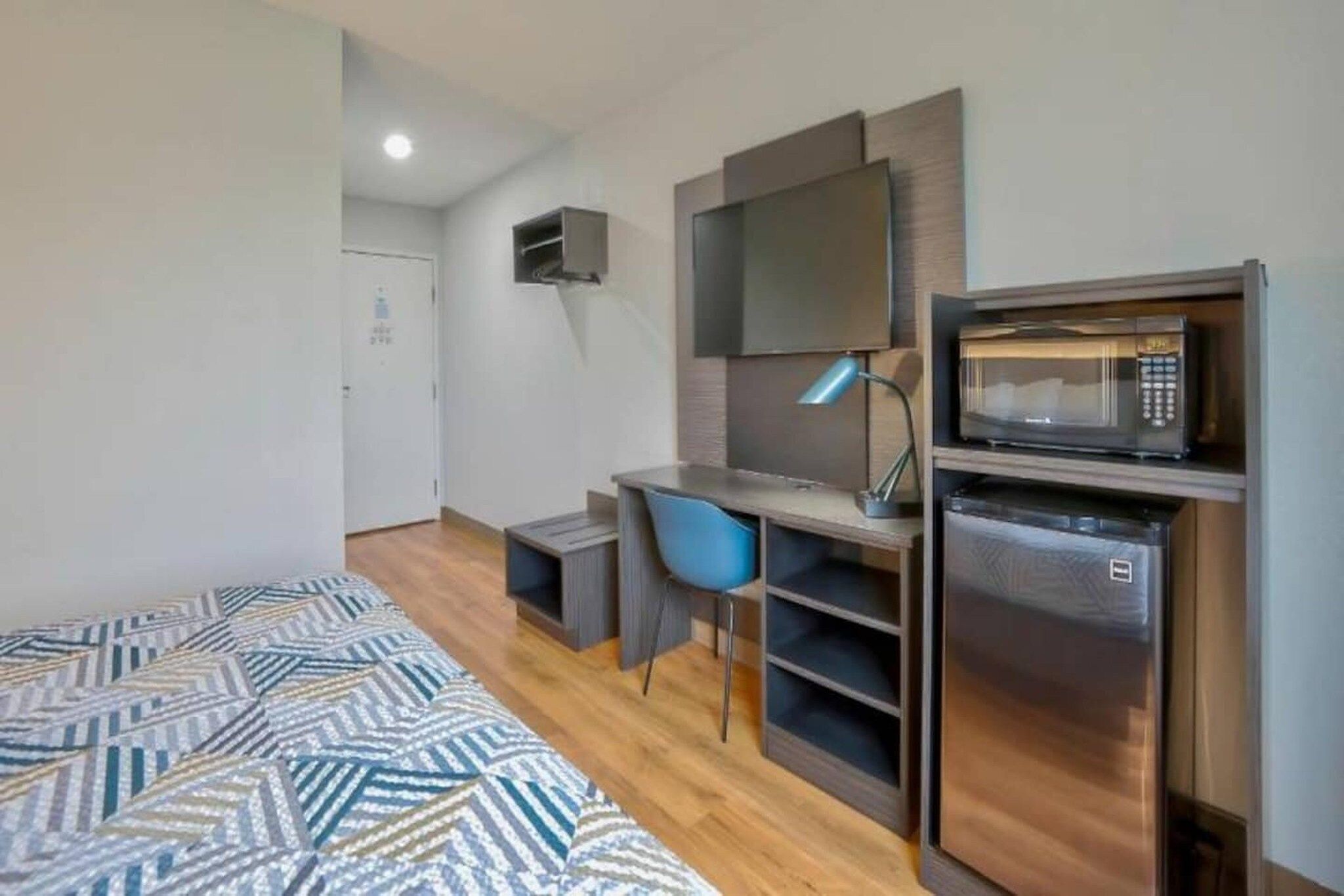 A compact room with a bed, a desk, a chair, a television, and a microwave.