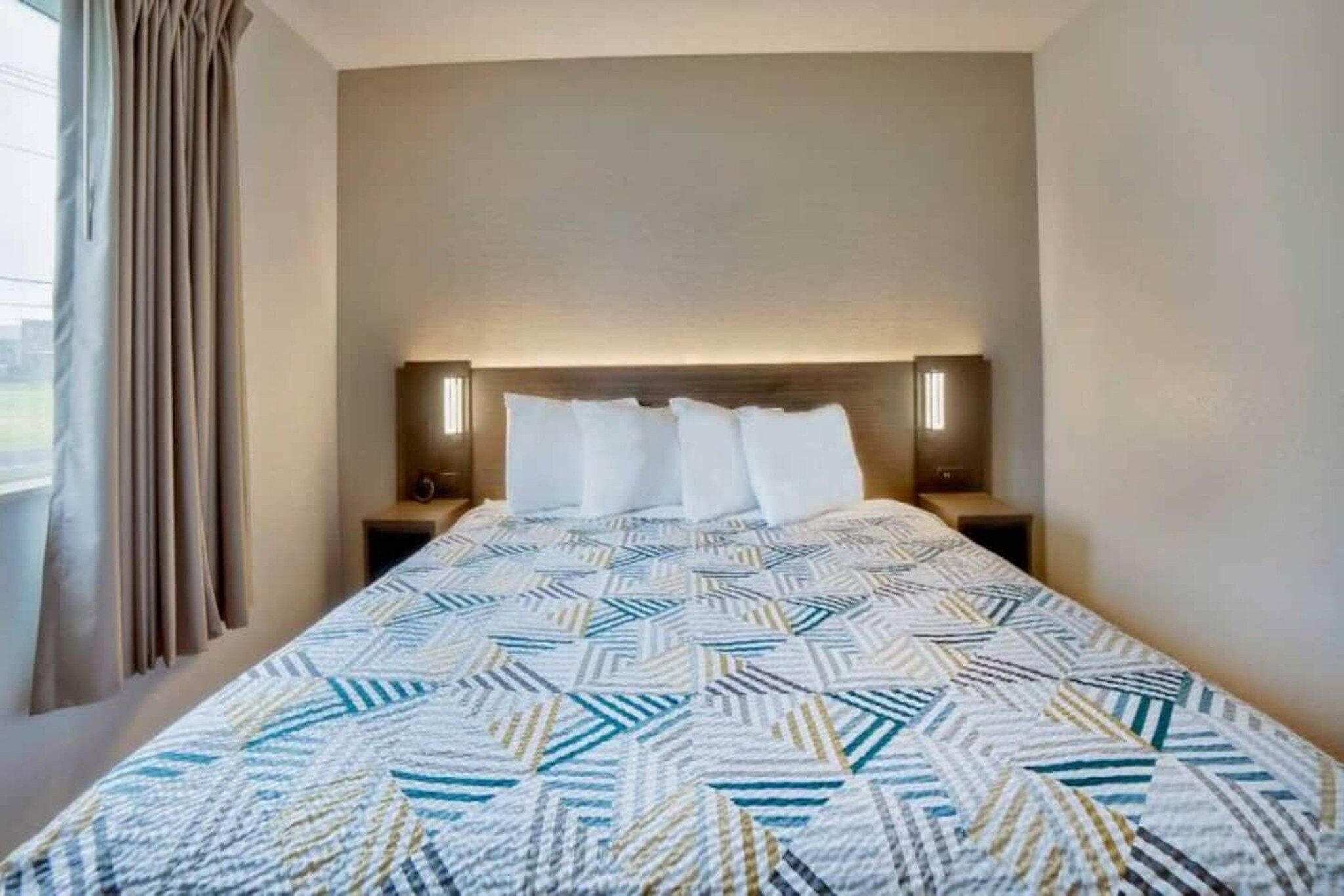 A hotel room with a bed, two bedside tables, a headboard, and curtains.