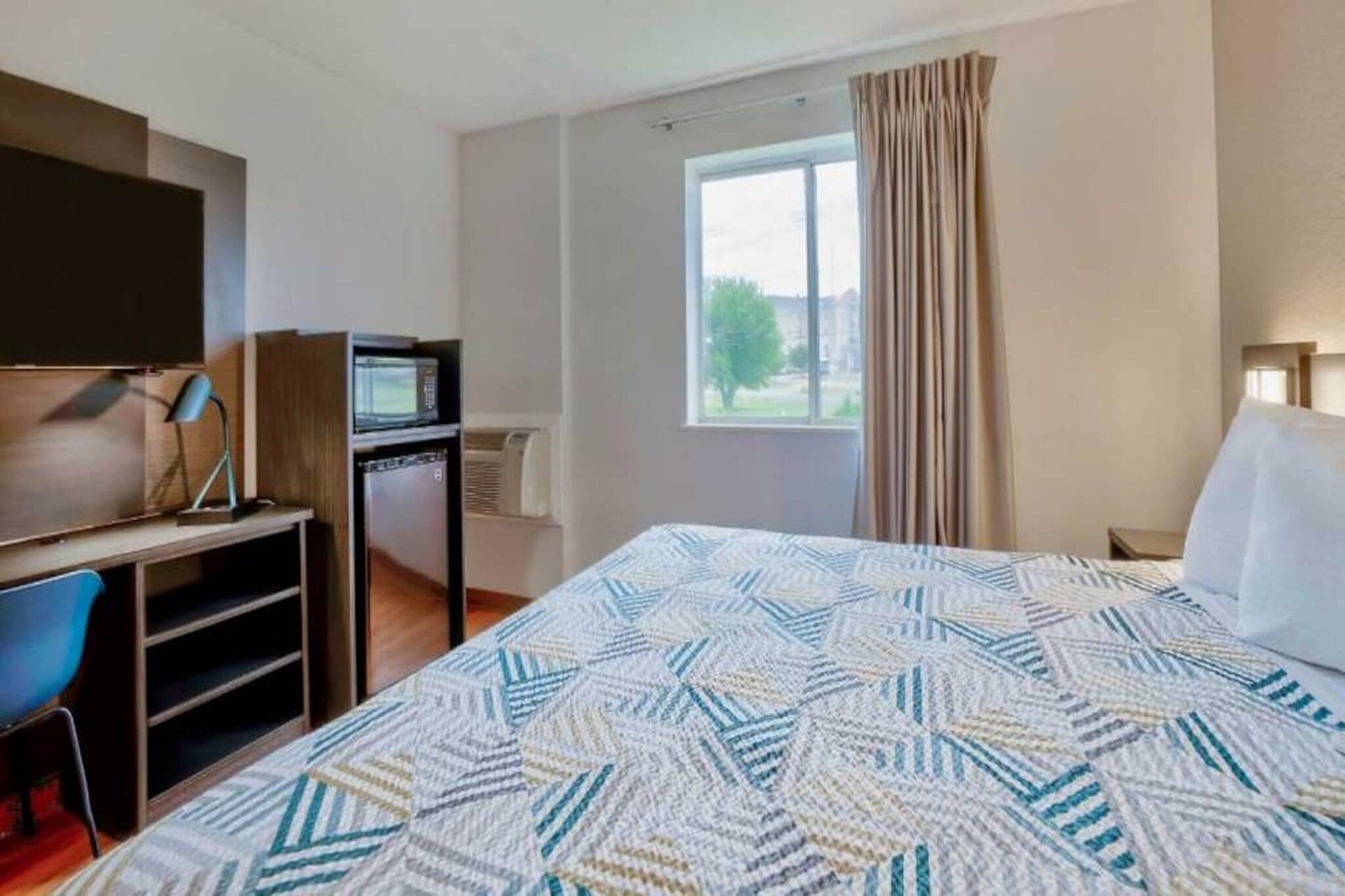A hotel room with a bed, a desk with a computer, a television, and a window with curtains.