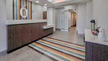 A hotel reception area with a modern design, a reception desk, a colorful striped carpet, and a coffee machine.