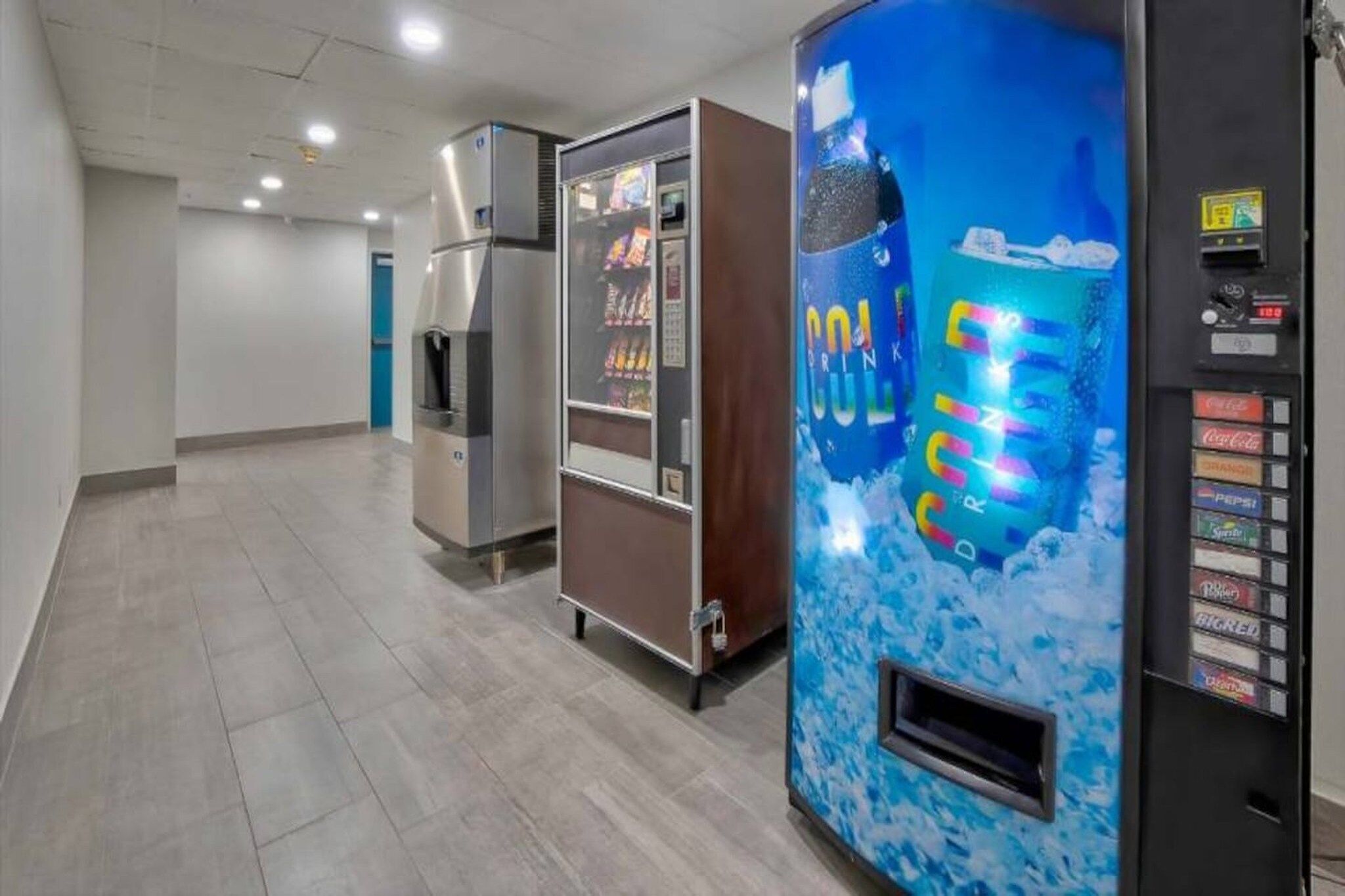 A corridor with vending machines, including a Coca-Cola cooler and a refrigerator.
