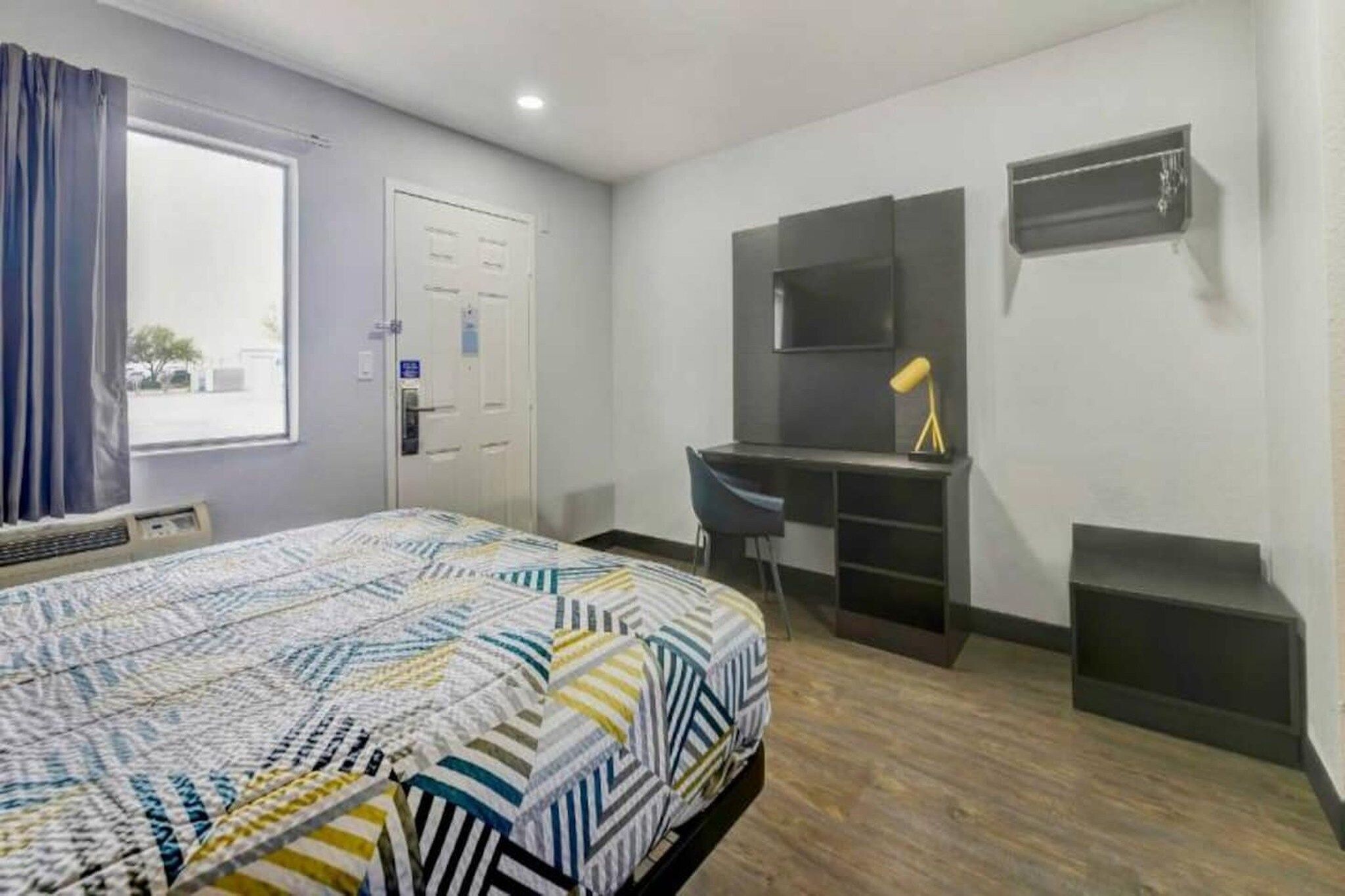A hotel room with a bed, a desk, a chair, a TV, and a window with curtains.