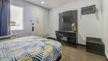 A hotel room with a bed, a desk, a chair, a TV, and a window with curtains.