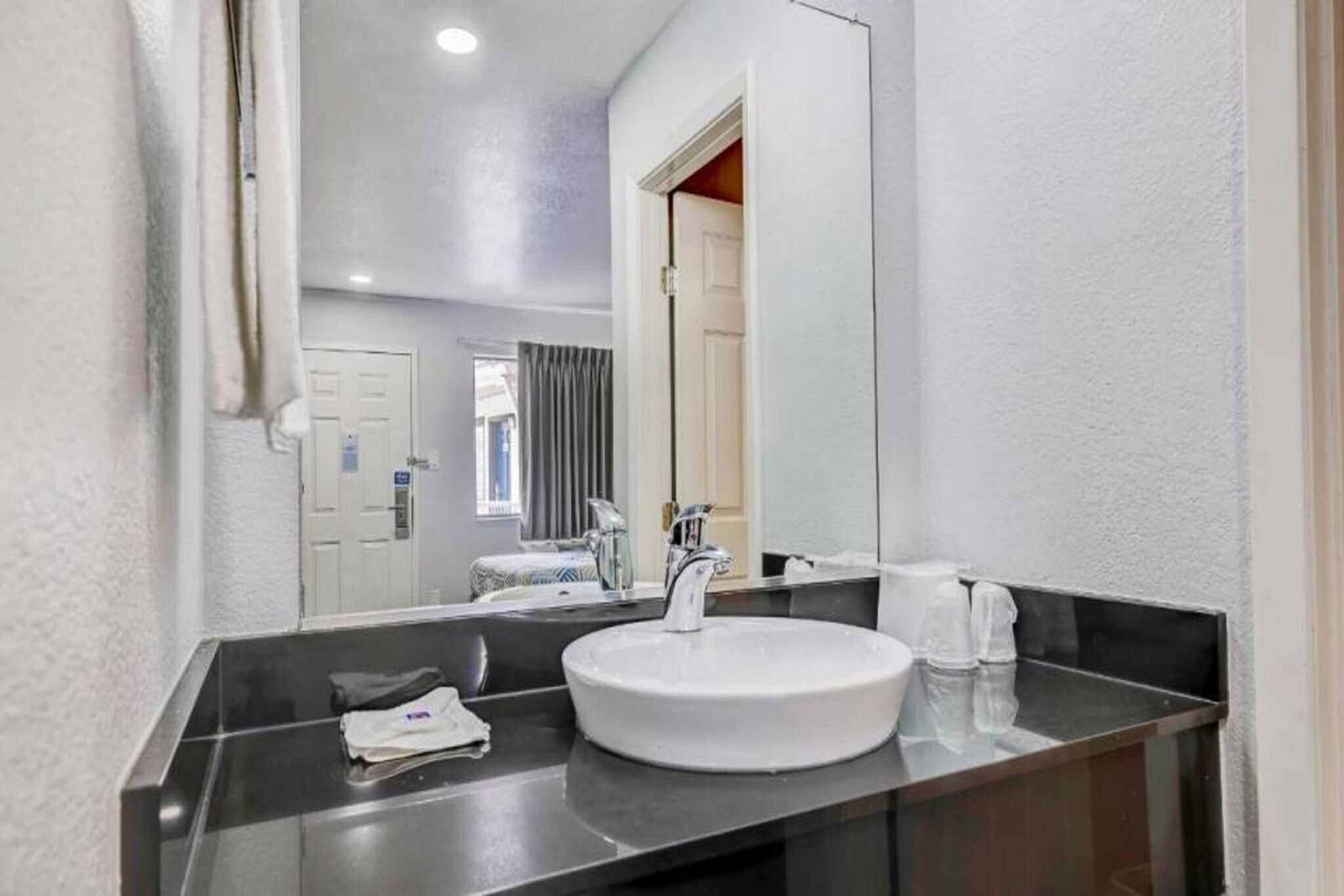 A hotel bathroom with a round sink, a mirror, and a towel dispenser.