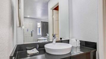A hotel bathroom with a round sink, a mirror, and a towel dispenser.