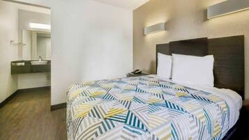 A hotel room with a bed, a nightstand, a mirror, and a bathroom visible in the background.