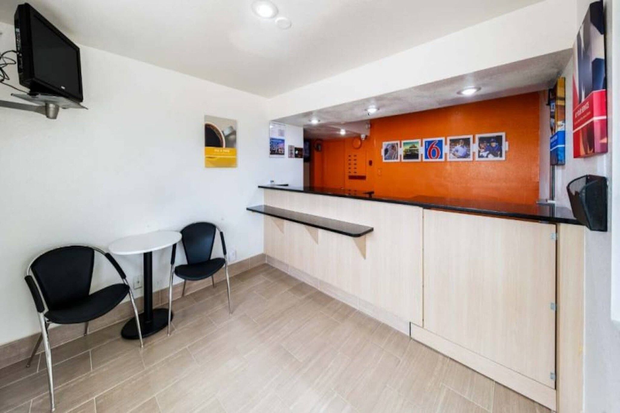 A small reception area with a counter, two chairs, a table, and a wall-mounted TV.