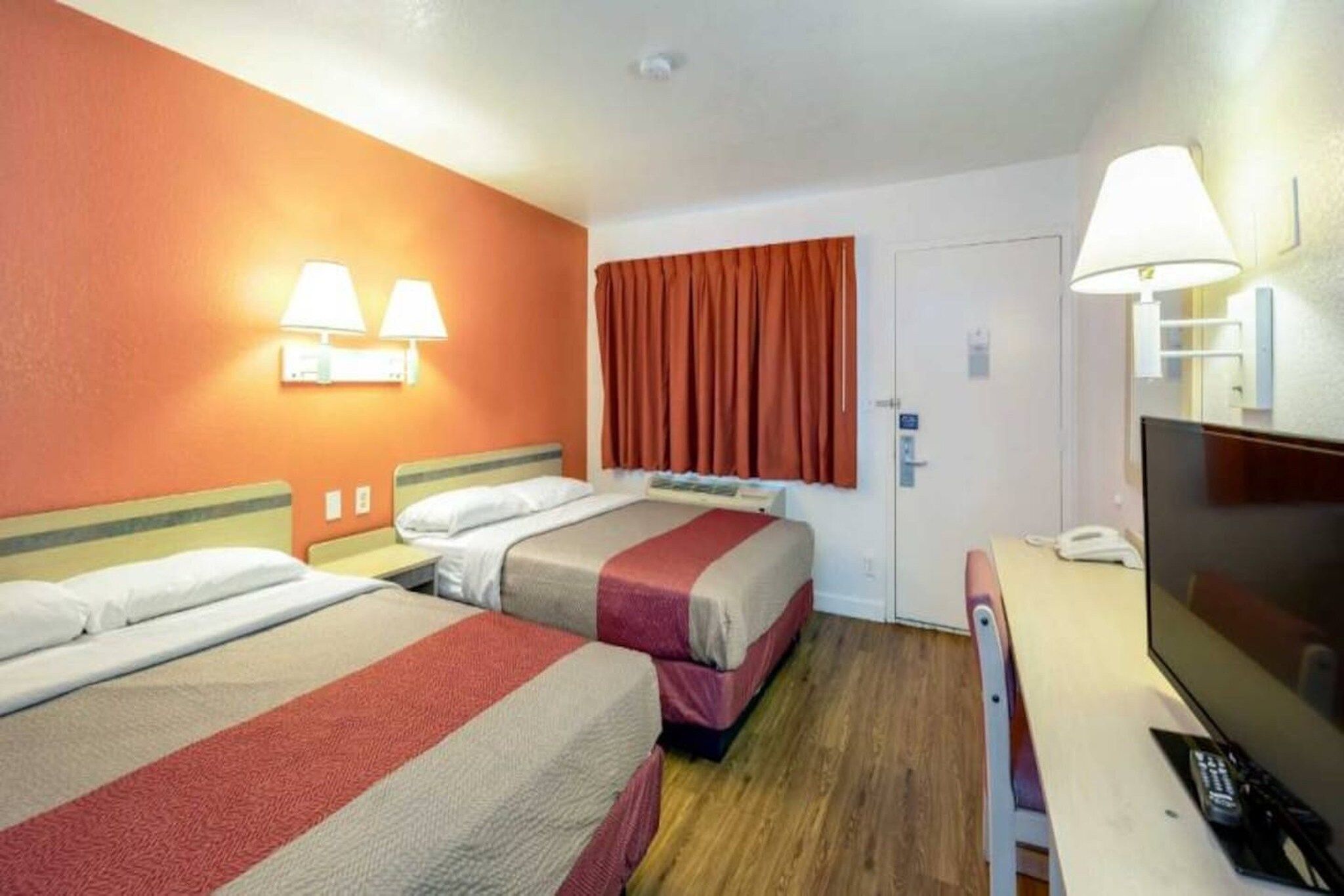 A hotel room with two beds, a television, and a door with a window.