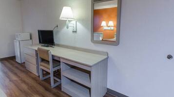 Een hotelkamer met een bureau, een stoel, een televisie, een magnetron en een bedlampje.