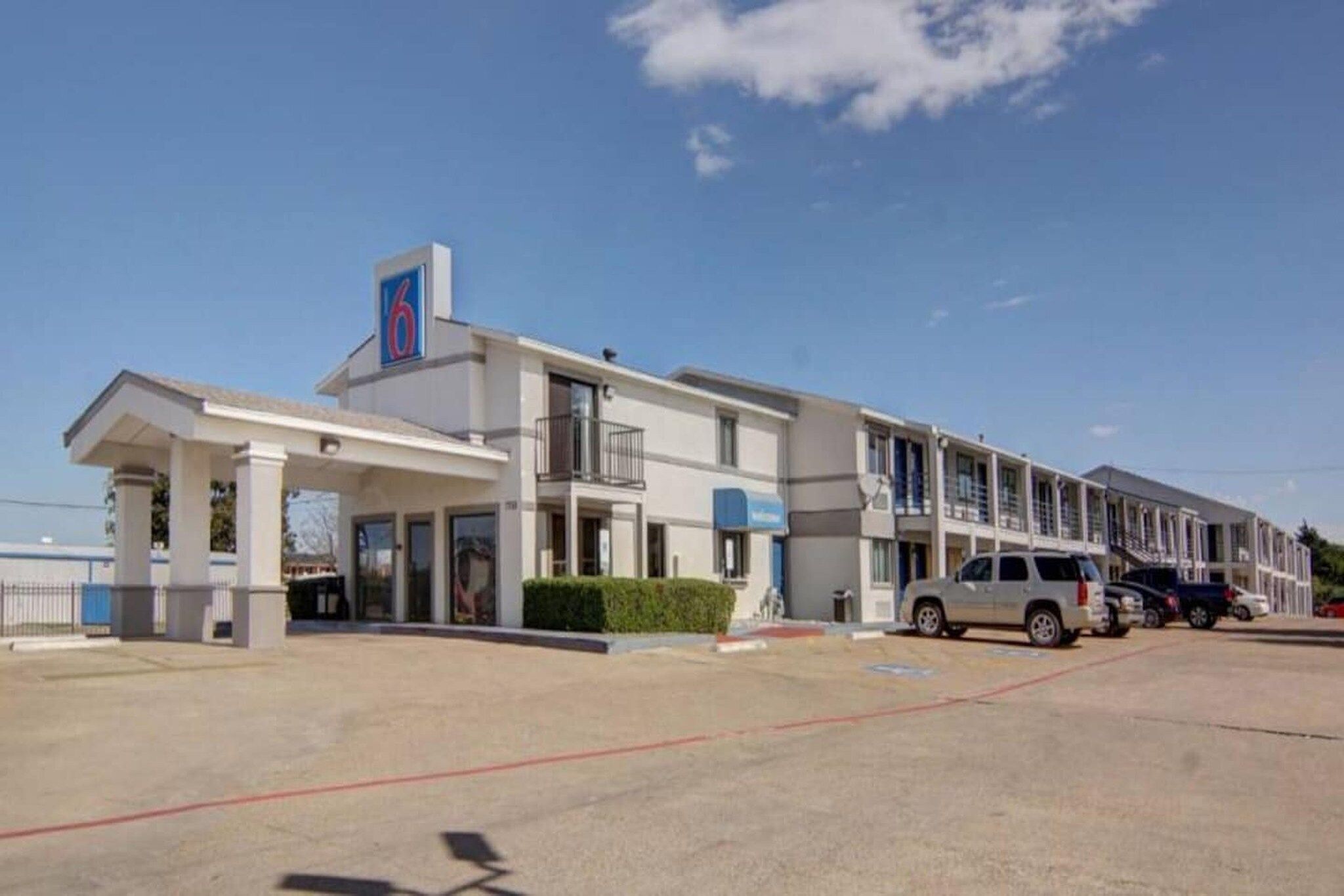 A motel with a large parking lot, a covered entrance, and a row of rooms.