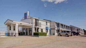 A motel with a large parking lot, a covered entrance, and a row of rooms.