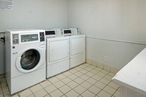 Een wasserette met een voorlader wasmachine en droger, een bedieningspaneel en een betegelde vloer.
