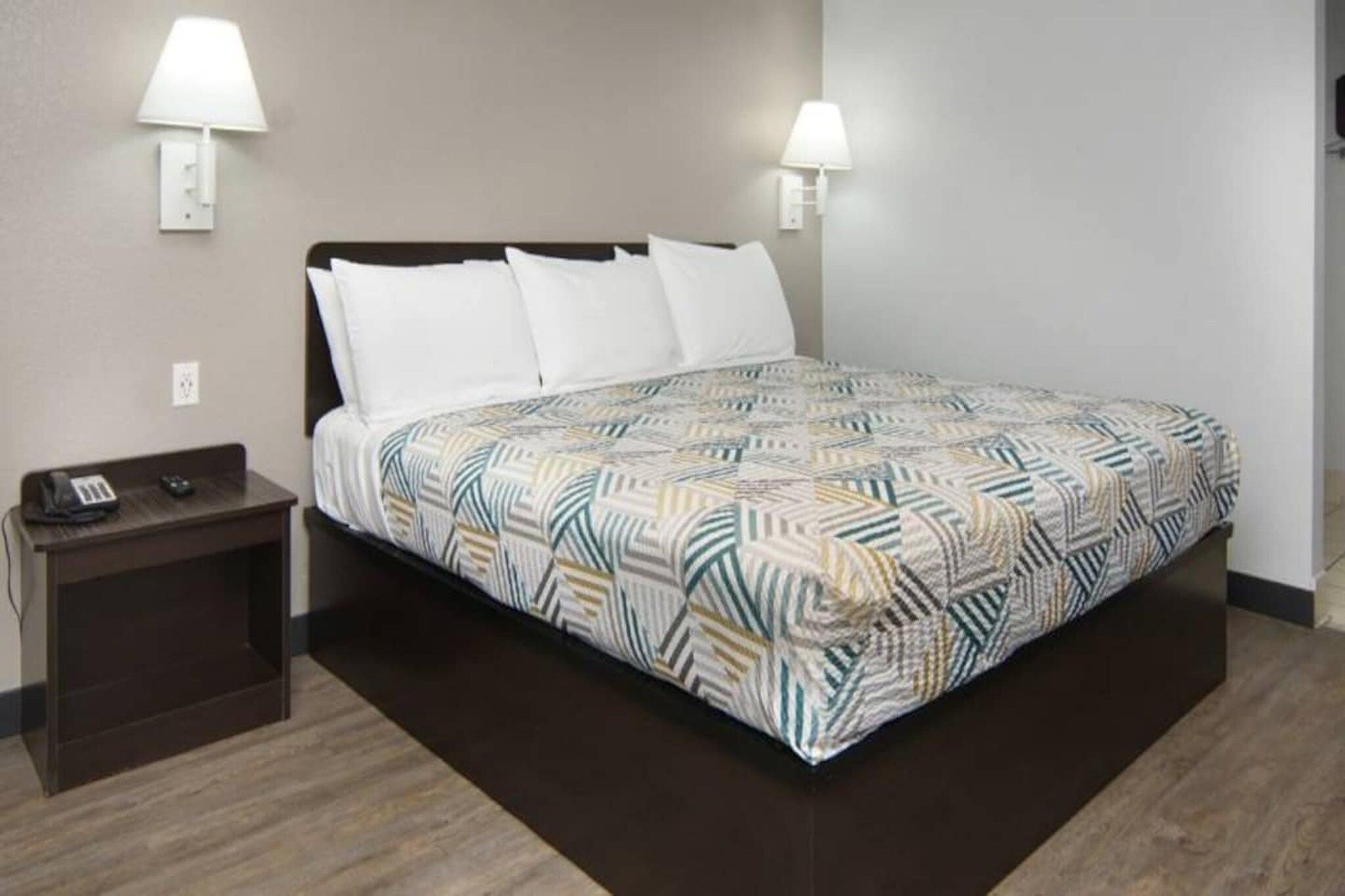 Habitación de hotel con cama, dos lámparas de noche, mesita de noche con teléfono y colcha estampada.