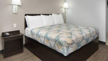 Habitación de hotel con cama, dos lámparas de noche, mesita de noche con teléfono y colcha estampada.