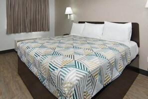A hotel room with a bed, a wall-mounted lamp, and a window with curtains. - 1 King Bed | Non-Smoking (LANCASTER)