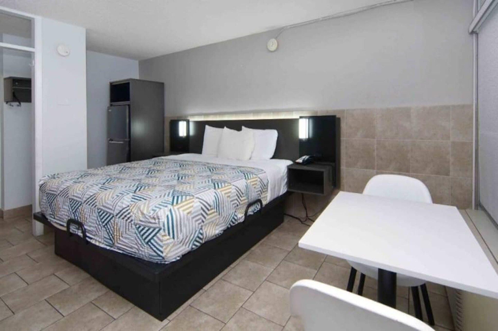 A hotel room with a bed, bedside table, nightstand, and a small table with chairs.