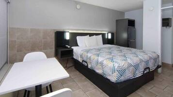 A hotel room with a bed, a desk, a chair, a nightstand, and a wardrobe.