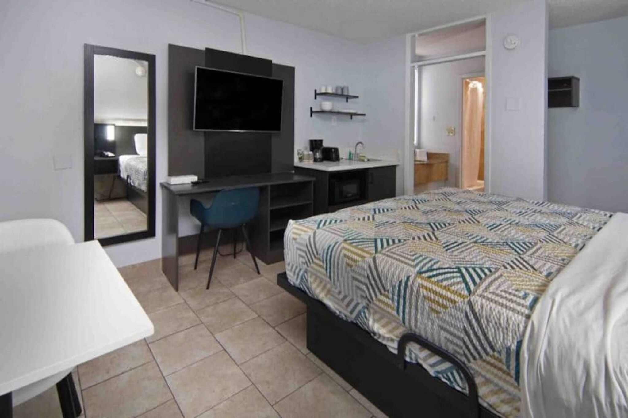 Een hotelkamer met een bed, een bureau, een stoel, een televisie en een spiegel.
