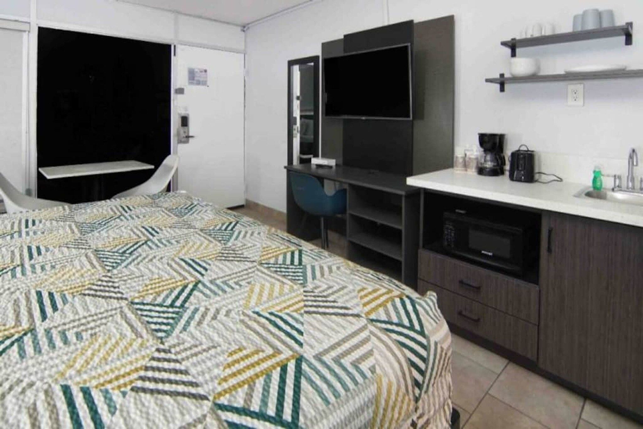 Een hotelkamer met een bed, een bureau, een flatscreen televisie, een magnetron en een koffiezetapparaat.
