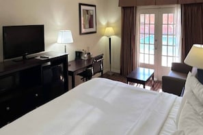 Ein Hotelzimmer mit Bett, Schreibtisch, Sessel, Fernseher und einem Fenster mit Vorhängen.
