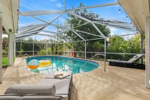 An indoor swimming pool with a glass enclosure, surrounded by lounge chairs and a sandy floor. - Tiki Sunset: Banana Riverfront Home w/ Dock, Saltwater Pool, Hot Tub & Tiki Bar in Cocoa Beach (Cocoa Beach)