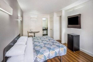 A hotel room with a bed, a small table, a chair, a TV, and a refrigerator. - 1 King Bed | Non-Smoking (Dallas)