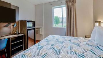 Habitación de hotel con cama, escritorio con computadora, televisor y ventana con cortinas.