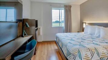Ein Hotelzimmer mit Bett, Schreibtisch, Stuhl, einem Fenster mit Vorhängen und Blick ins Freie.