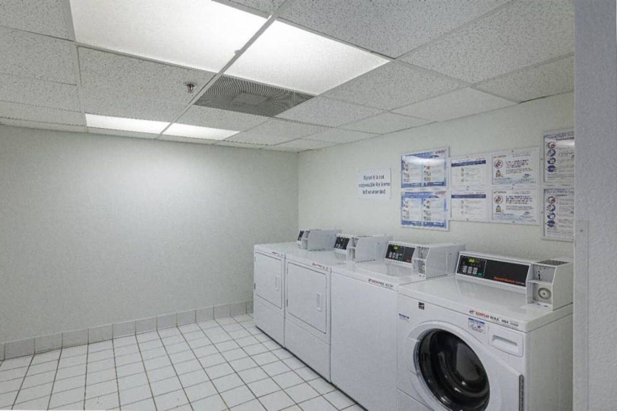 A laundry room with a washing machine and dryer, tiled floor, and informational posters on the wall.