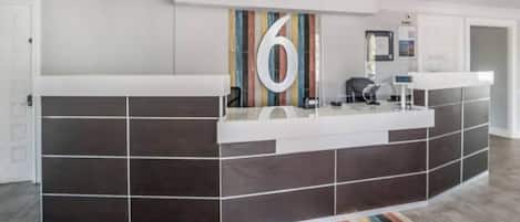 Een receptiebalie met een groot cijfer '6' erboven, een glazen scheidingswand en een kleurrijk gestreept tapijt op de vloer.