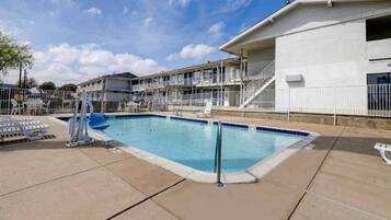 A swimming pool with a lifeguard stand, lounge chairs, and a building with multiple balconies in the background.