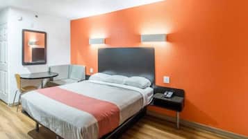 A hotel room with a bed, bedside table, chair, and a small round table.
