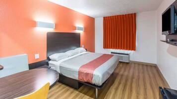 A hotel room with a bed, a desk, a chair, a TV, and a window with curtains.