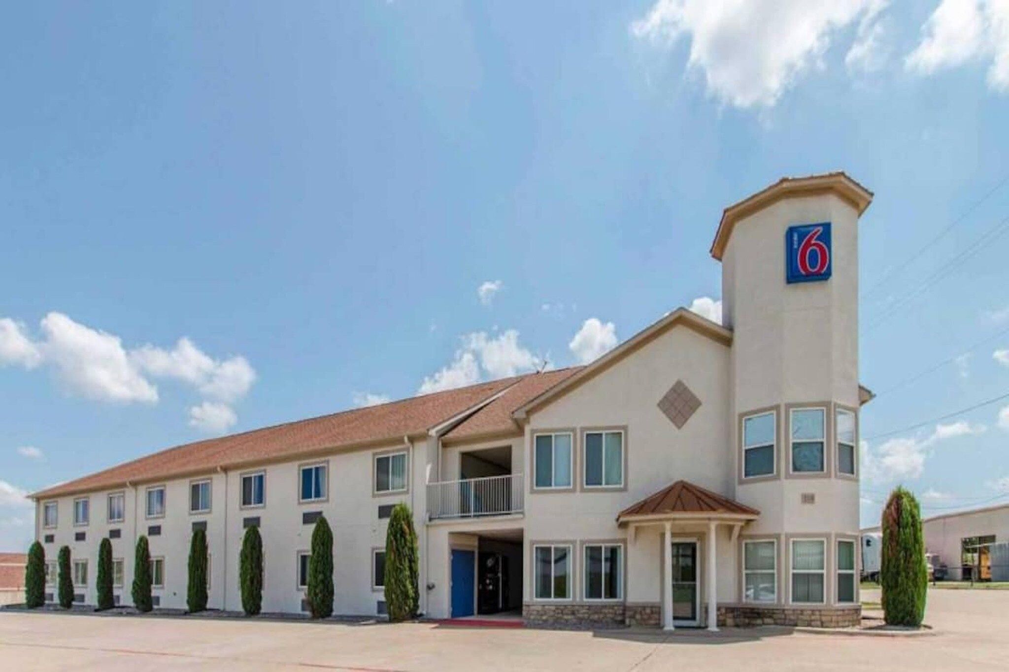 A multi-story hotel with a prominent '6' sign on the corner, a flat roof, and a series of windows.