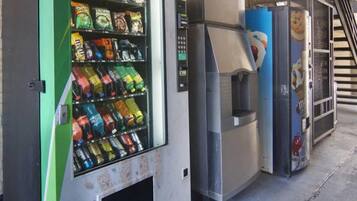 A vending machine with various snacks and drinks, a self-service beverage dispenser, and a trash bin.