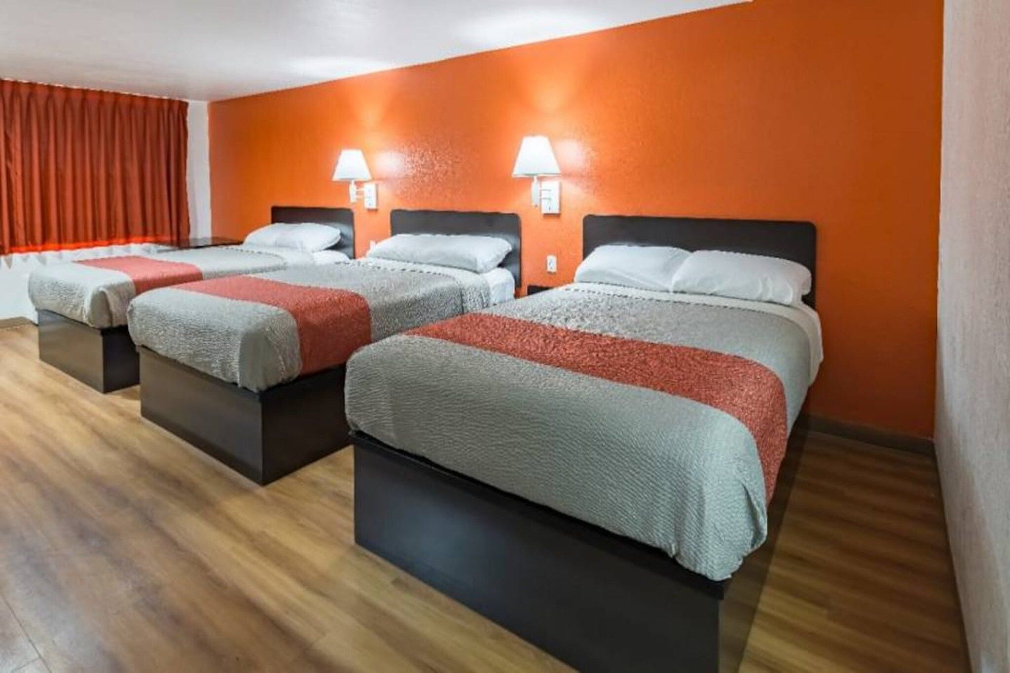 Une chambre d’hôtel avec trois lits, chacun doté d’une tête de lit, un mur rouge et un plancher en bois.