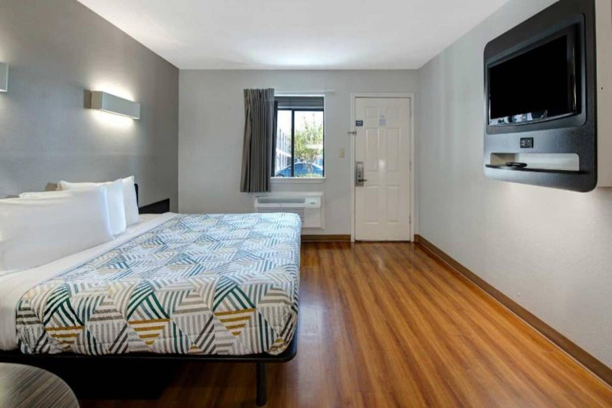 Ein Hotelzimmer mit einem Bett, einem Fernseher, einem Fenster mit Vorhängen und einer Tür.