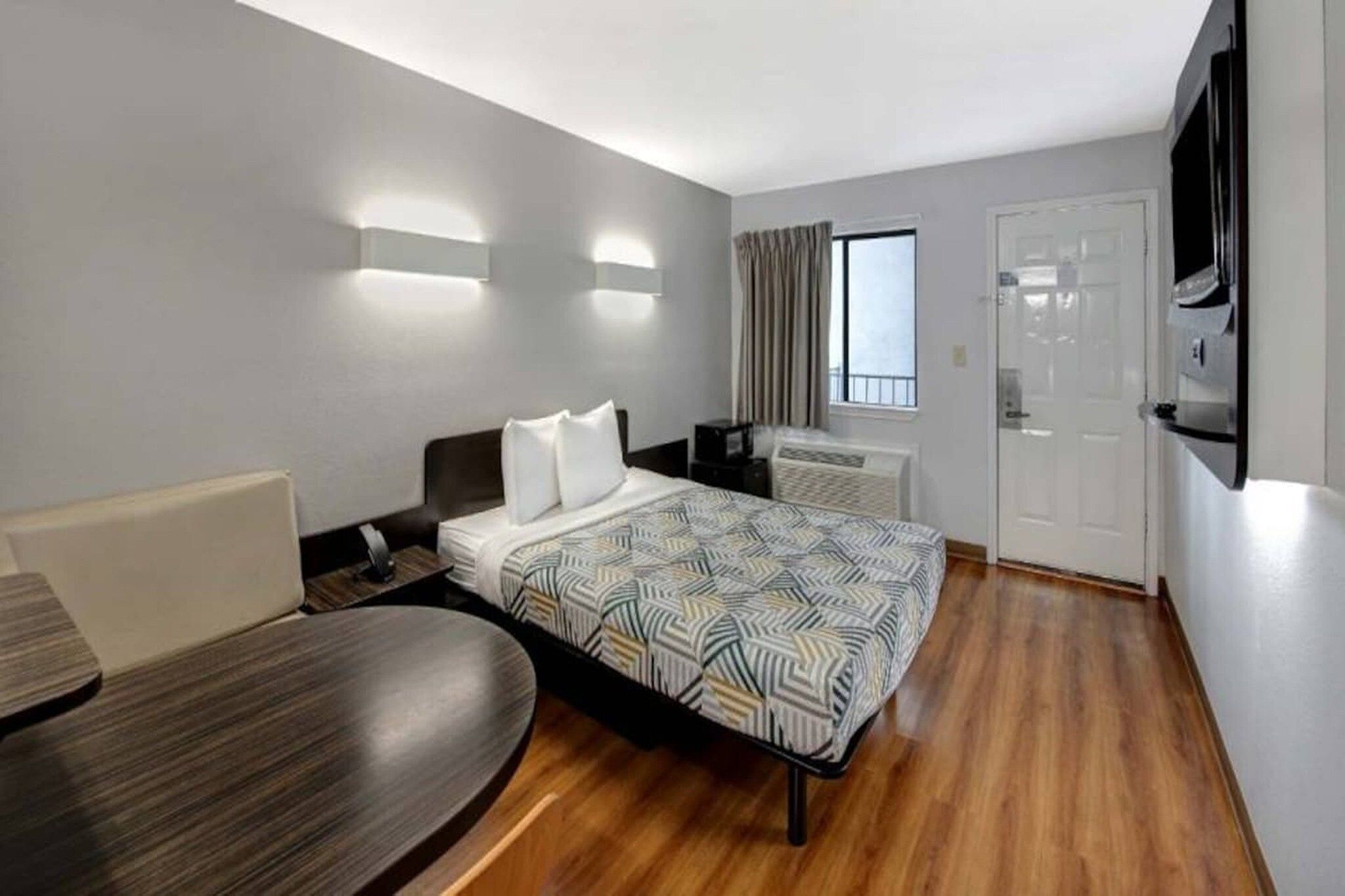 Een hotelkamer met een bed, een bureau, een stoel, een televisie en een raam met gordijnen.