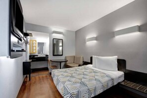 Habitación de hotel con cama, escritorio, silla, espejo y lámpara de pared.