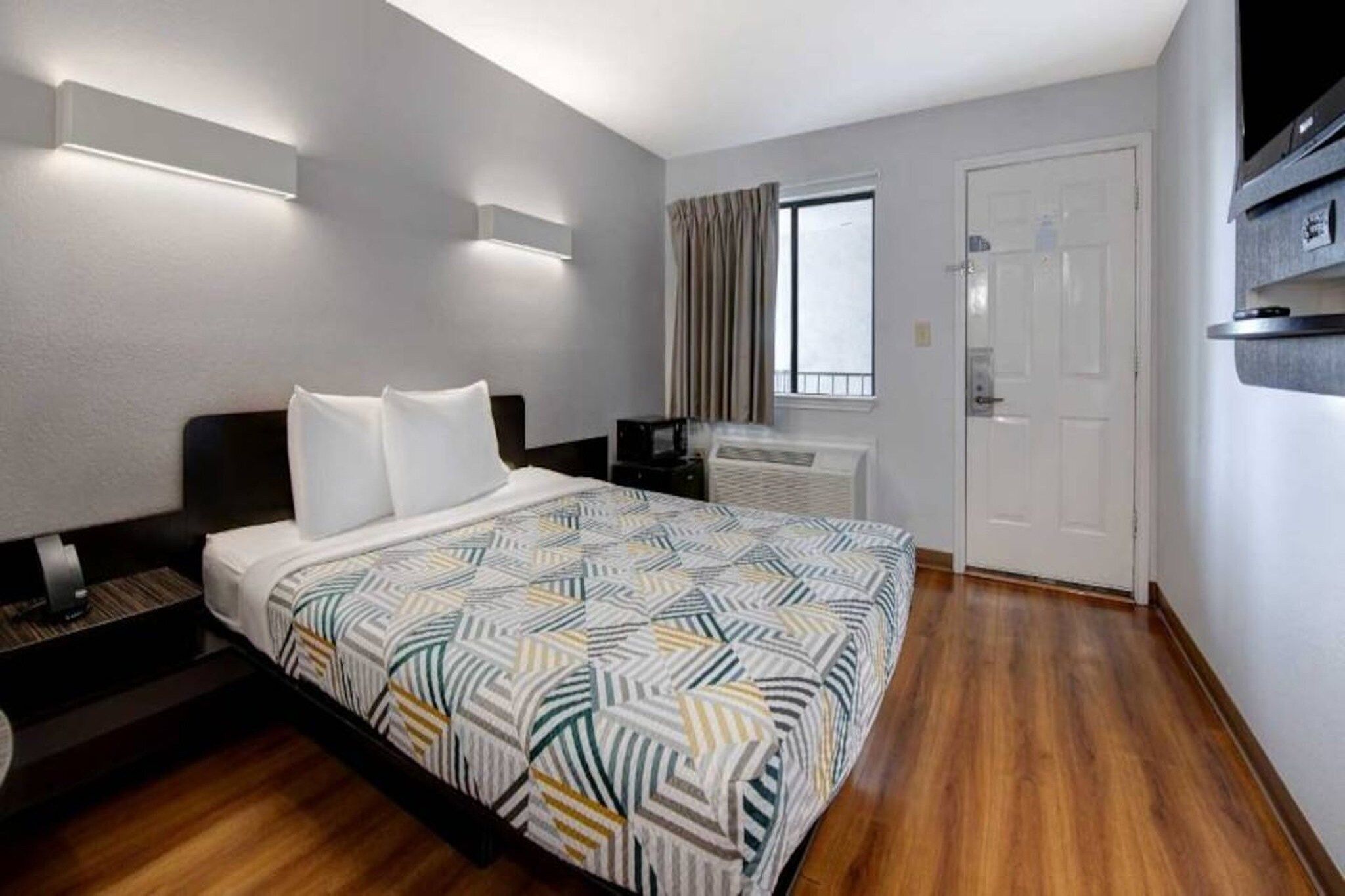 Habitació d'hotel amb llit, taules de nit, finestra amb cortines, radiador i porta.