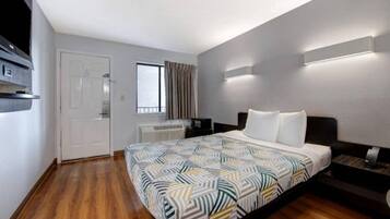 A hotel room with a bed, a desk, a chair, a window with curtains, and a door.