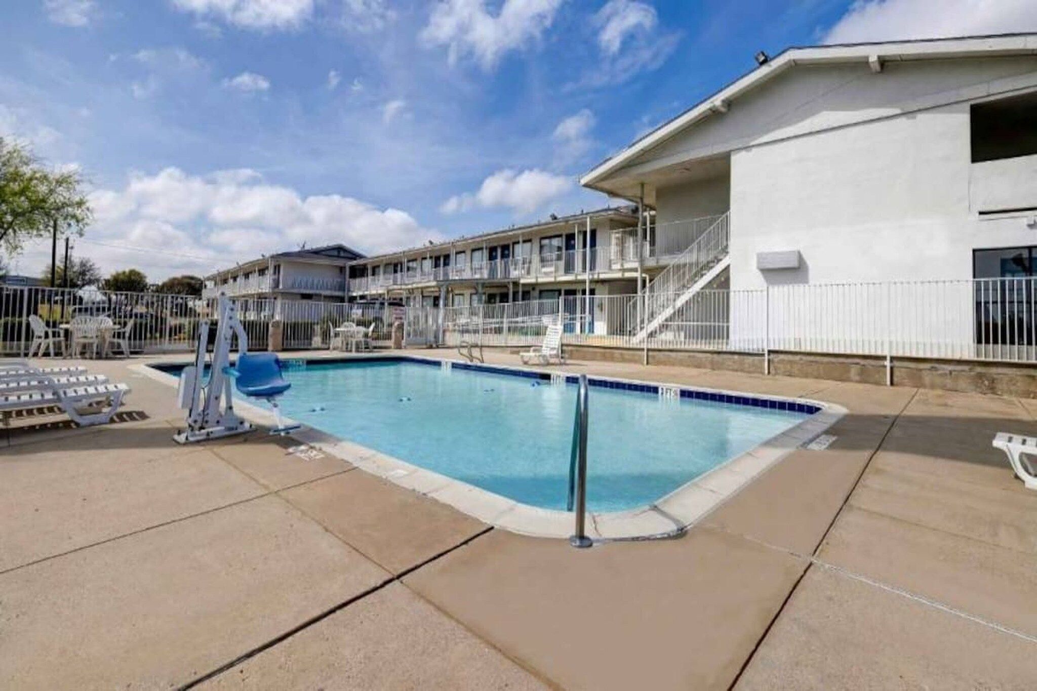 A swimming pool with a lifeguard stand, lounge chairs, and a building with multiple balconies in the background.