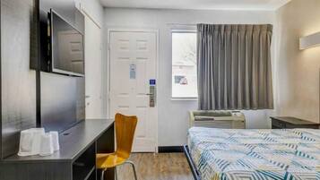 A hotel room with a bed, a desk, a chair, a television, a window with curtains, and a door.