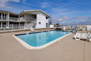 A swimming pool with lounge chairs and a building with a balcony.