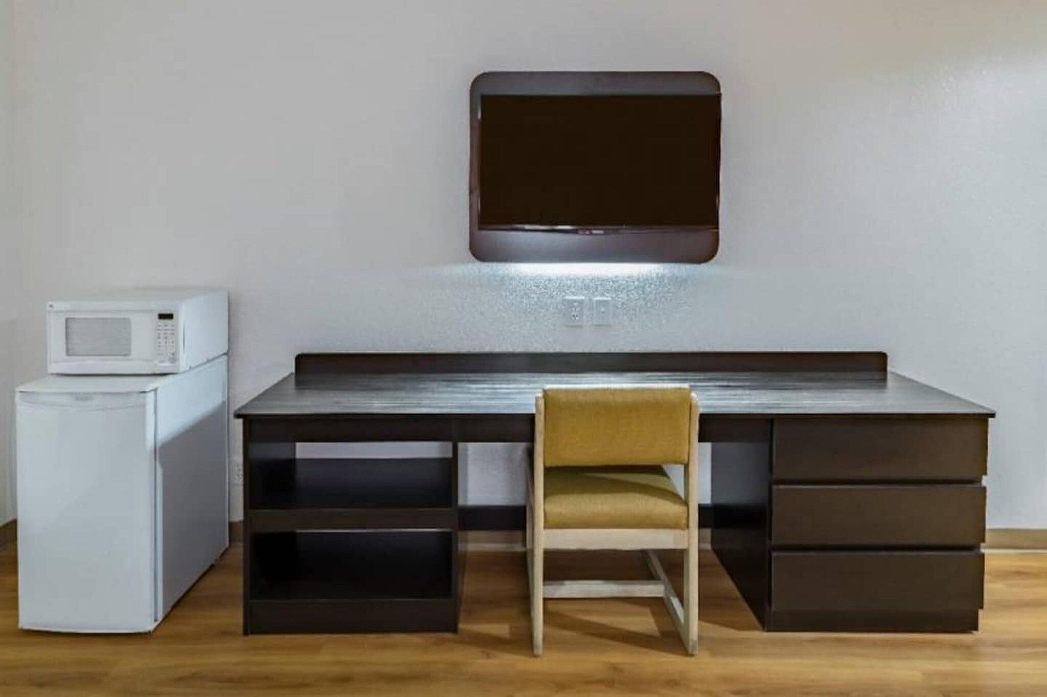 Un espace de travail compact comprenant un bureau, une chaise et un four à micro-ondes.