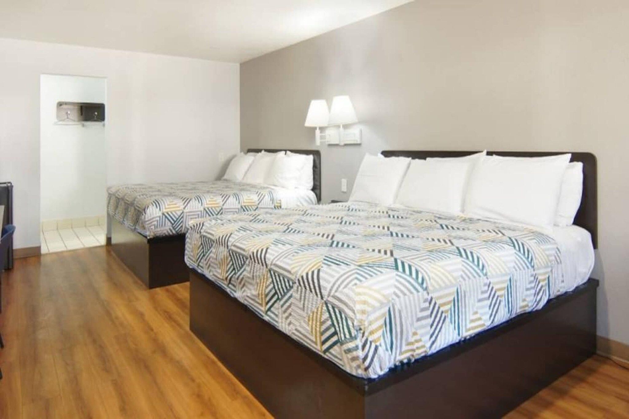A hotel room with two beds, wooden flooring, and a mirror on the wall.